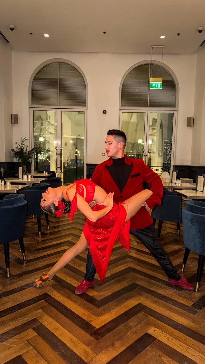 Salsa dancer in a red jacket dipping his partner in a red fringe dress